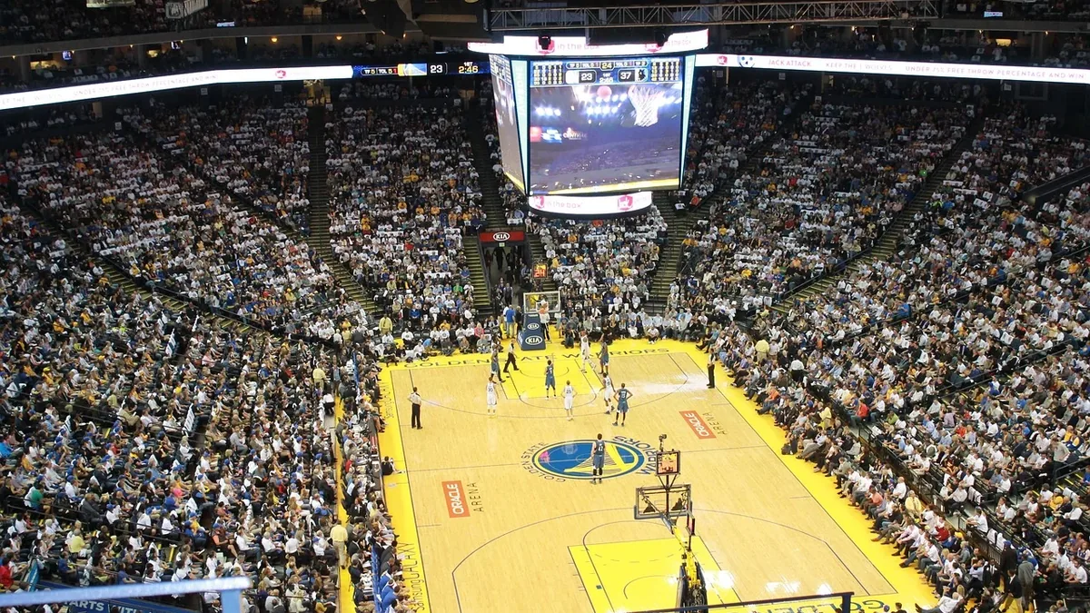 A basketball game in progress at a packed arena, with the court and players prominently visible.