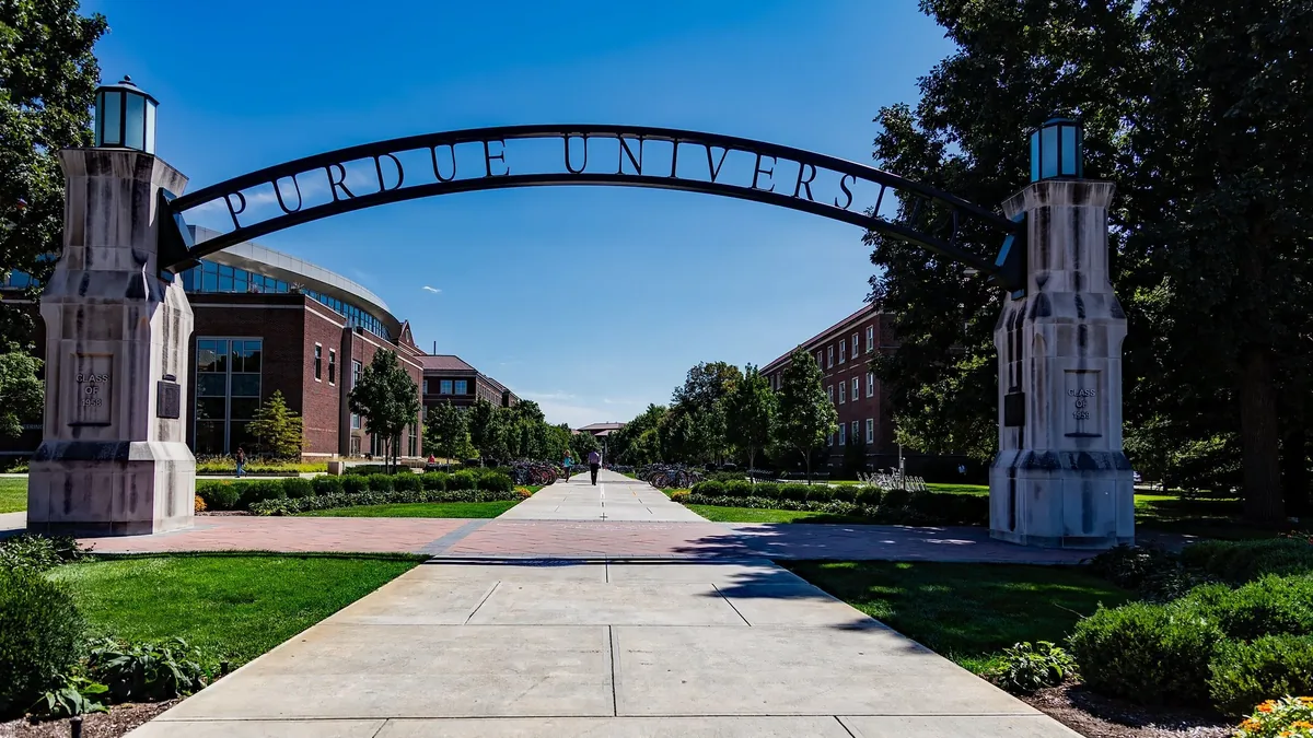 The Purdue University campus, featuring a large archway with the university's name, a long sidewalk, and a building in the background.